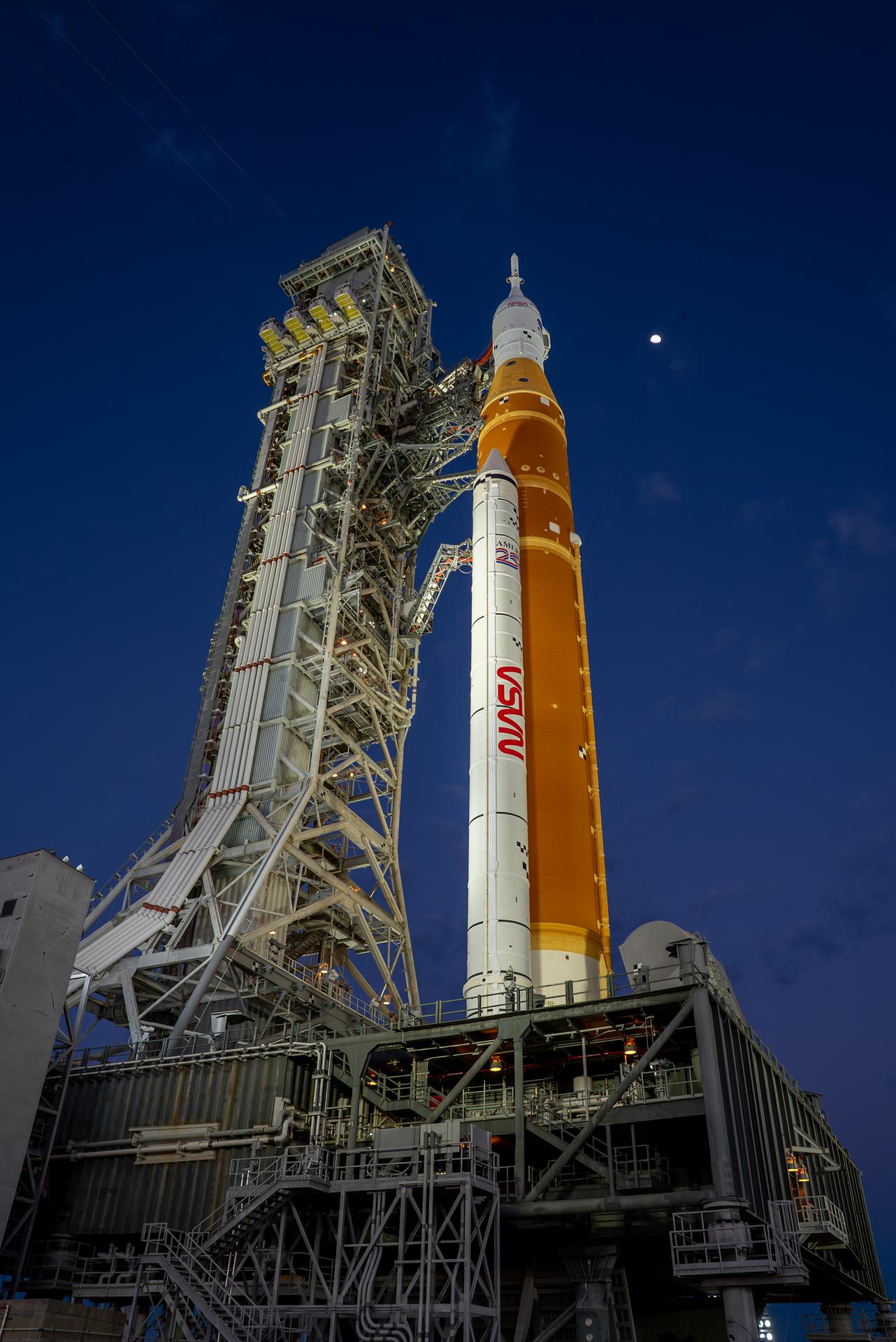 The Moon is seen shining over the SLS (Space Launch System) and Orion spacecraft, atop the mobile launcher on January 28, 2026. The rocket is currently at Launch Pad 39B at NASA’s Kennedy Space Center in Florida, as teams are preparing for a wet dress rehearsal to practice timelines and procedures for the launch of Artemis II.